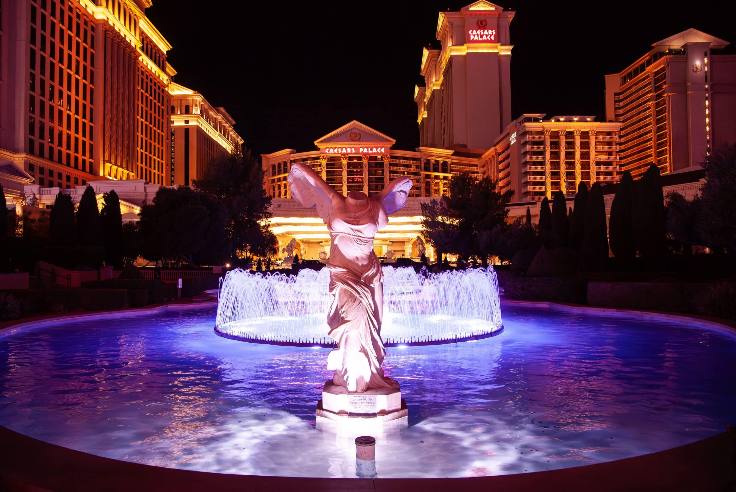 Caesars Palace lit at night behind the winged Victory statue and fountain on the Las Vegas Strip