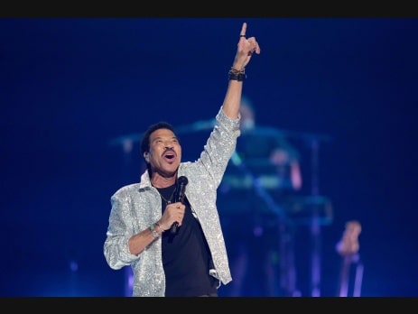 Lionel Richie performing in a silver sequined jacket and pointing skyward during a Las Vegas concert