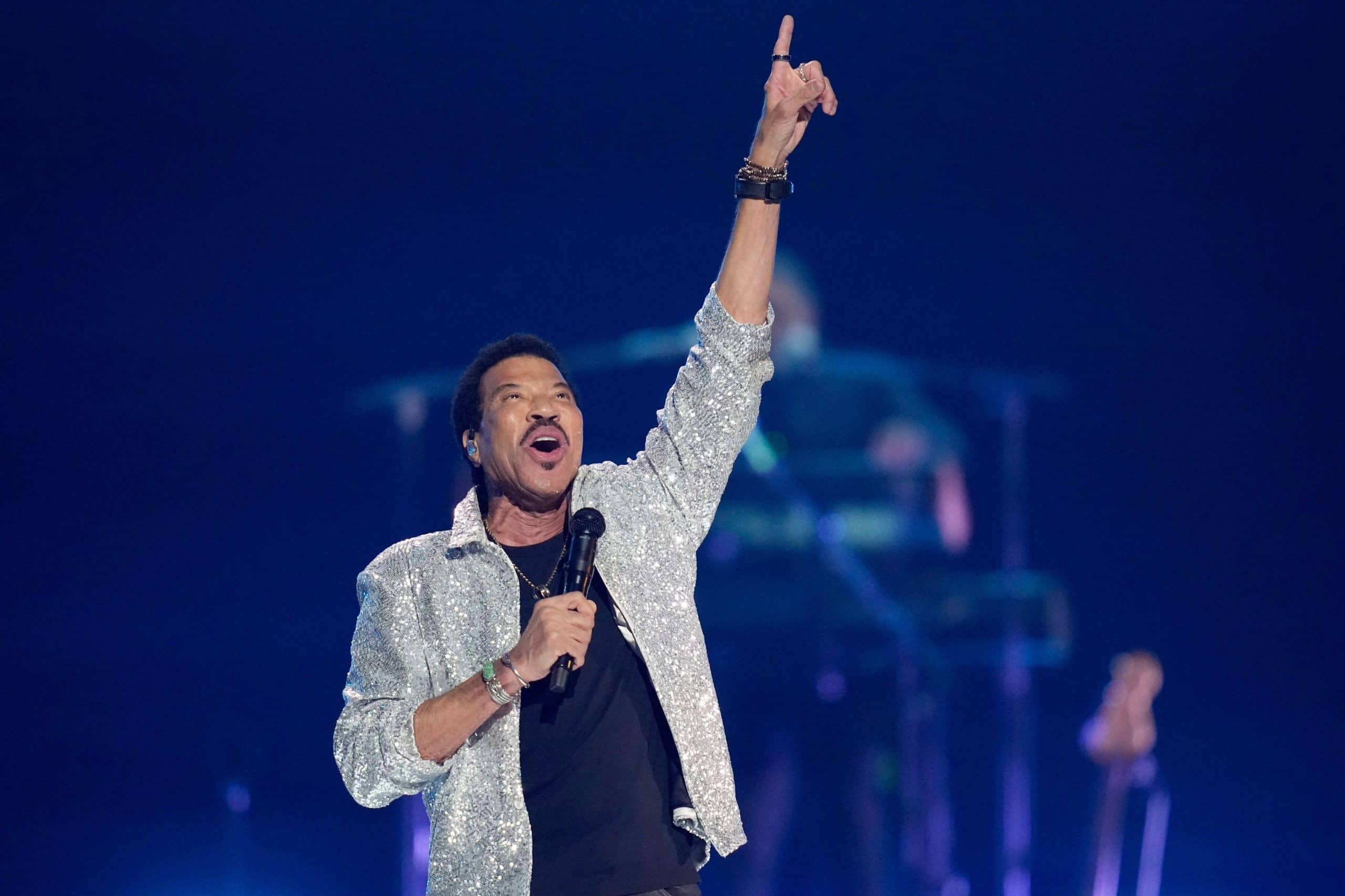 Lionel Richie performing in a silver sequined jacket and pointing skyward during a Las Vegas concert