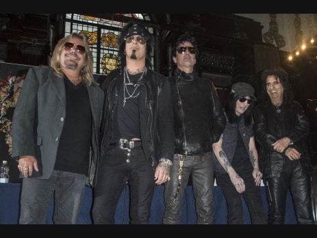 The five members of Motley Crue standing together in a row in sunglasses and black leather in front of a stained-glass window