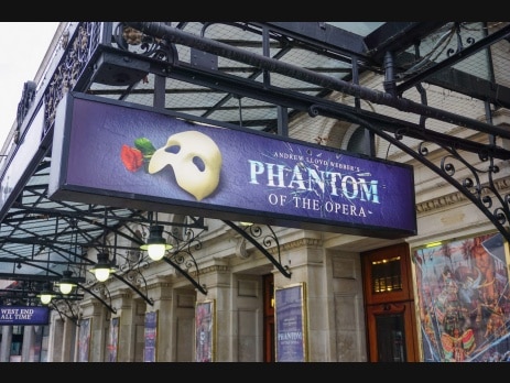 Purple theatre marquee sign reading Andrew Lloyd Webber's Phantom of the Opera, beside a white half mask and a red rose