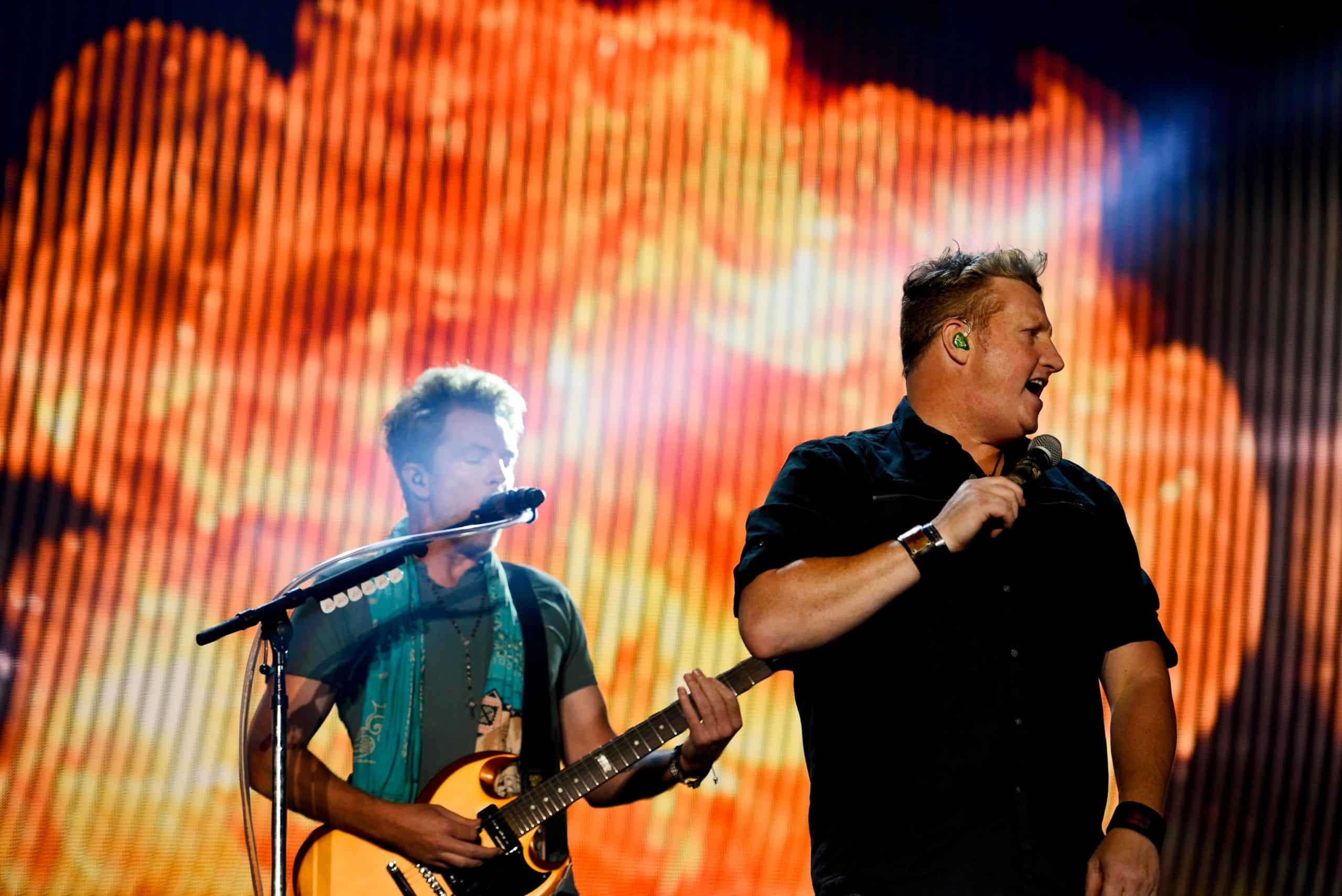Rascal Flatts performing live, singing and playing guitar on a brightly lit stage
