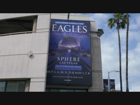 Eagles concert banner advertising the band's Sphere Las Vegas residency, with the venue's dome visible behind desert road art