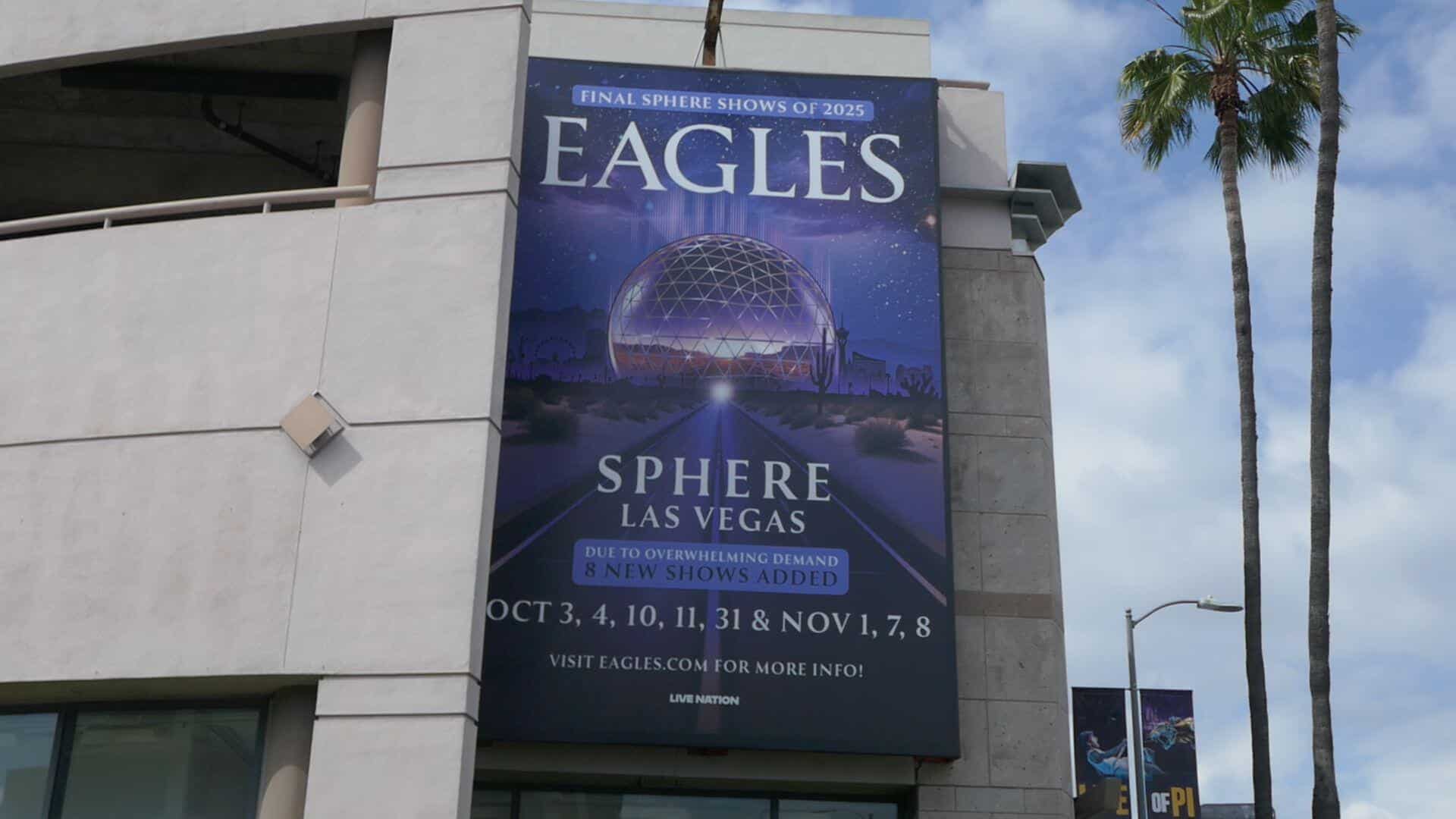 Eagles concert banner advertising the band's Sphere Las Vegas residency, with the venue's dome visible behind desert road art