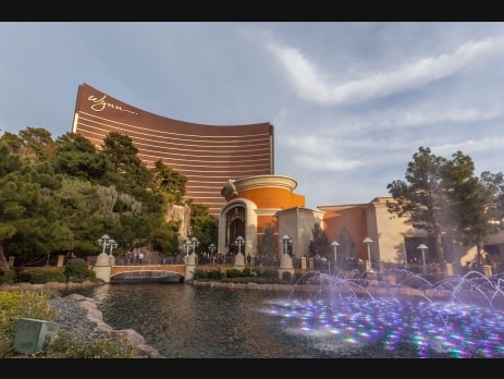 The curved bronze Wynn Las Vegas hotel tower with illuminated fountains in the foreground