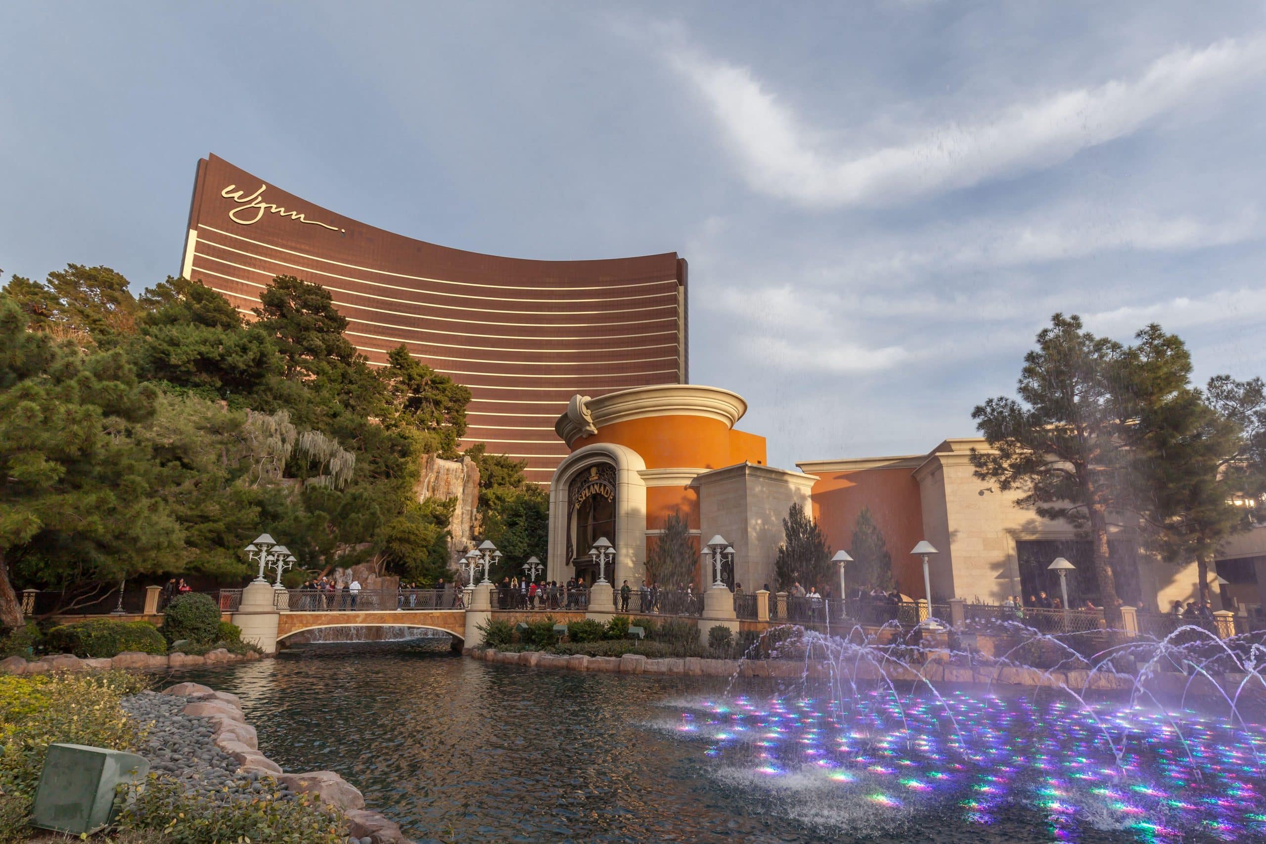 The curved bronze Wynn Las Vegas hotel tower with illuminated fountains in the foreground