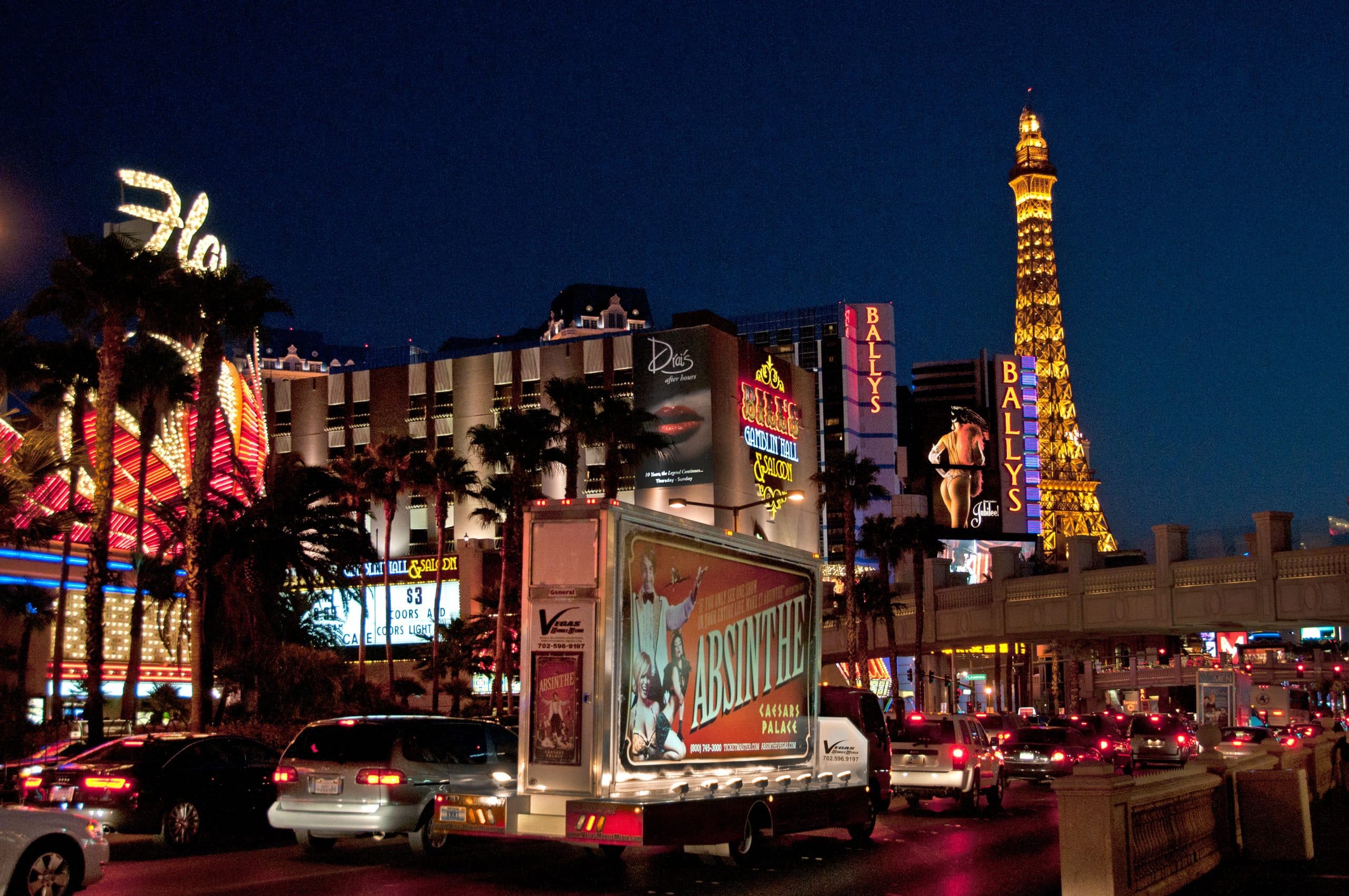Mobile Absinthe Las Vegas advertising truck on the Strip at night with casino neon signs and the Paris Las Vegas Eiffel Tower replica in the background