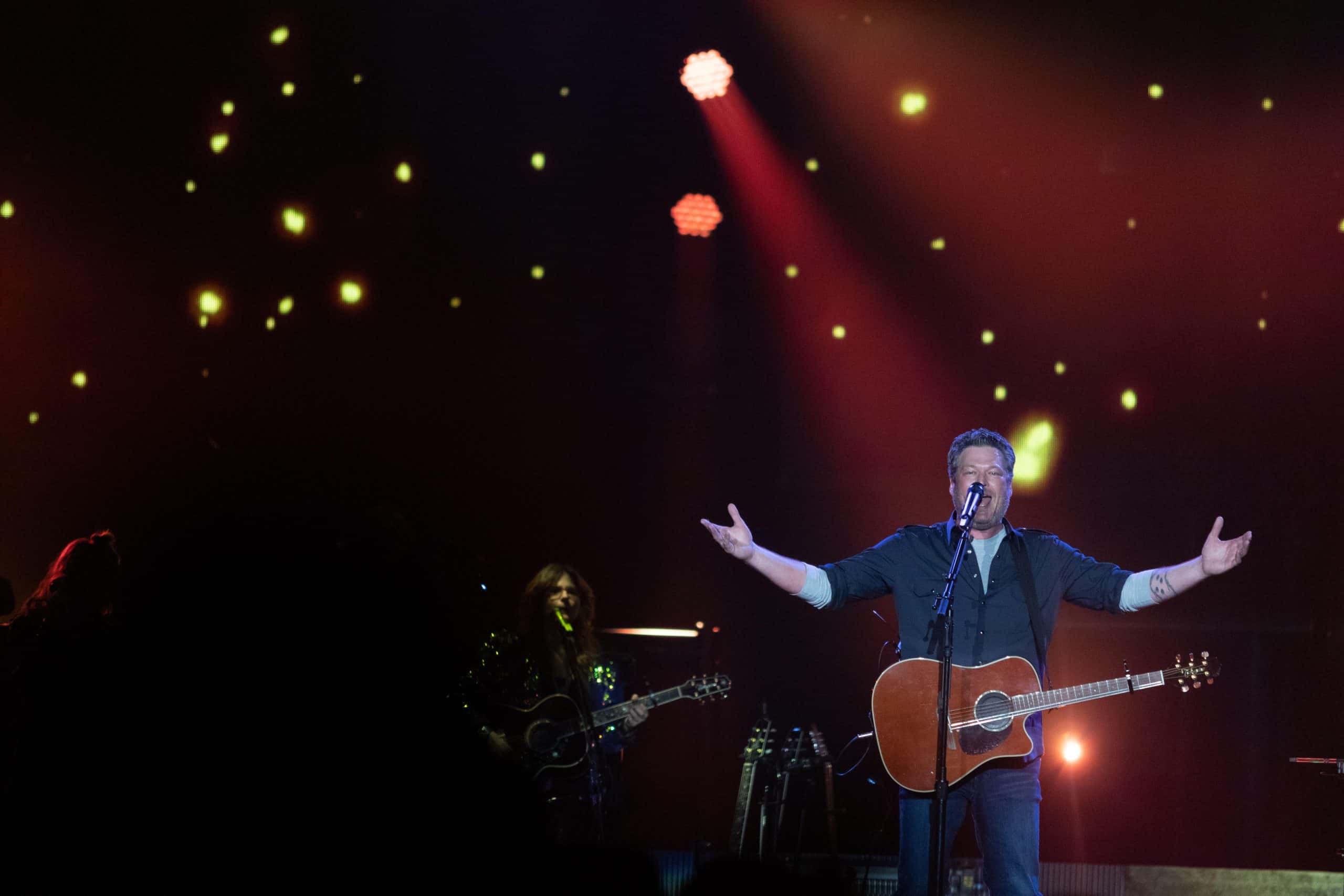 Blake Shelton performing on stage with his acoustic guitar at a Las Vegas concert, arms outstretched