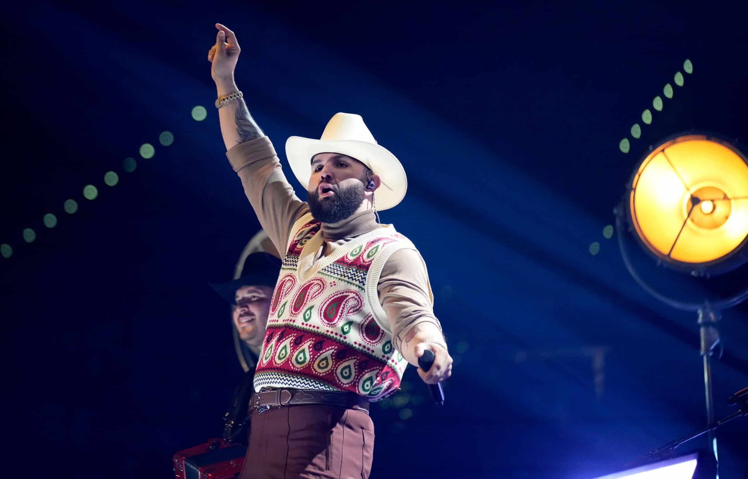 Carin Leon performing live on stage in his signature white cowboy hat at a concert