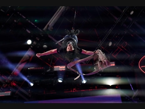 Criss Angel performing an aerial stunt suspended upside down above the stage with dramatic blue and red stage lighting