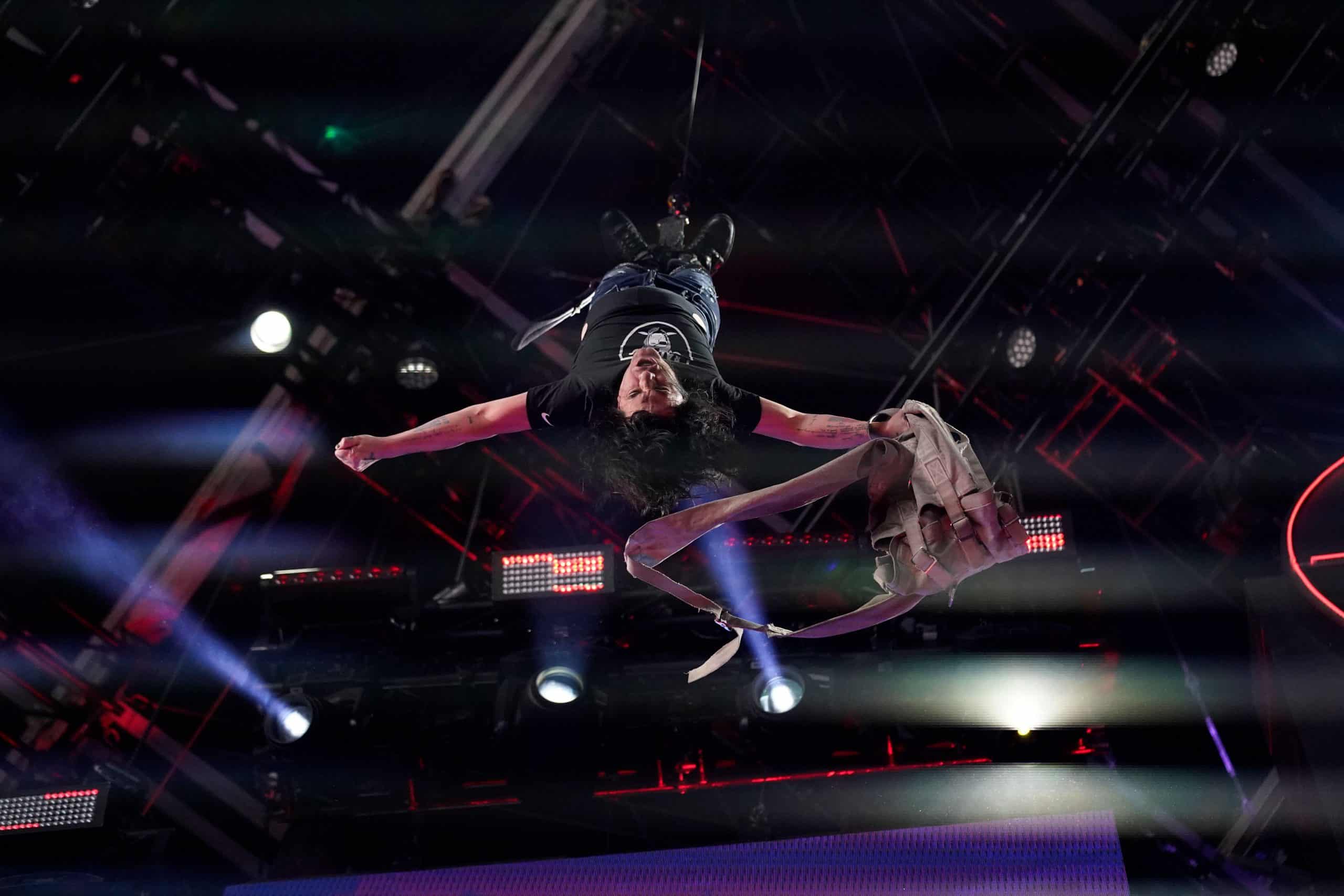 Criss Angel performing an aerial stunt suspended upside down above the stage with dramatic blue and red stage lighting