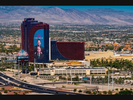 The Rio All-Suite Hotel tower in Las Vegas wrapped with a large Penn and Teller advertisement, with the resort marquee and desert mountains in the background