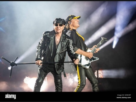 Scorpions perform live, vocalist at the mic stand beside a guitarist with a white guitar under stage lights