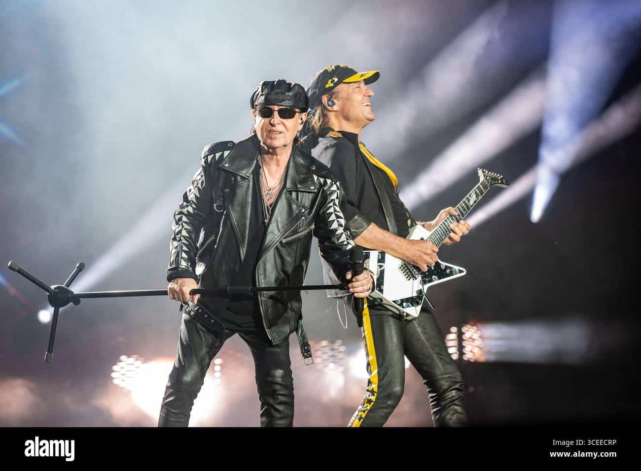 Scorpions perform live, vocalist at the mic stand beside a guitarist with a white guitar under stage lights